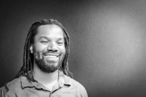 A man with dreads smiling for the camera.