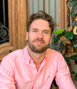 A man in pink shirt sitting next to a tree.